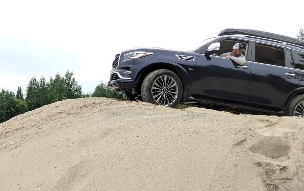 An INFINITI QX80 SUV driving up a sand dune.