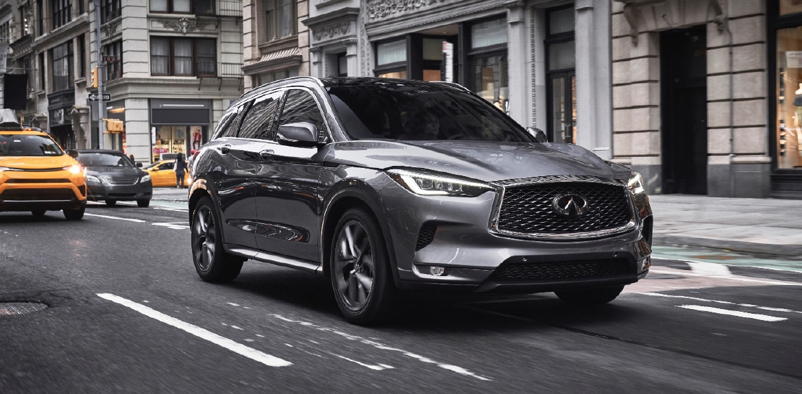 Desktop 1920 x 1080 wallpaper image of a grey QX50 Luxury Crossover driving down city street.