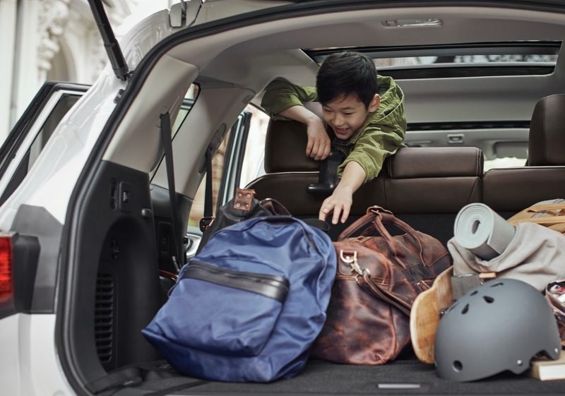 A boy in the 2nd row of an INFINITI QX60 reaching for his backpack in the spacious cargo area | Finding The Most Spacious SUV