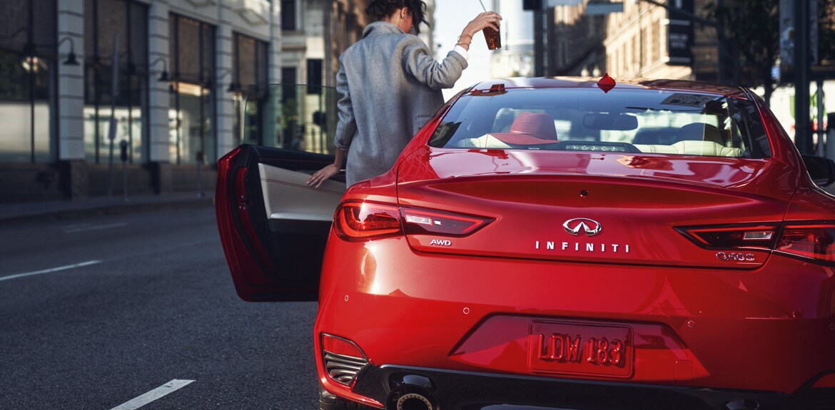 Rear view of a woman entering her car which is a red 2022 INFINITI Q60 S sports coupe