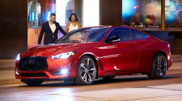 A couple walking towards a shiny red 2022 INFINITI Q60 Coupe parked on the side of the road.