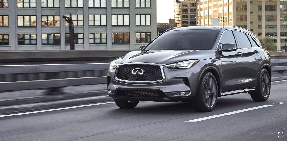 Side and front profile of a Graphite Shadow 2022 INFINITI QX50 driving fast on the road
