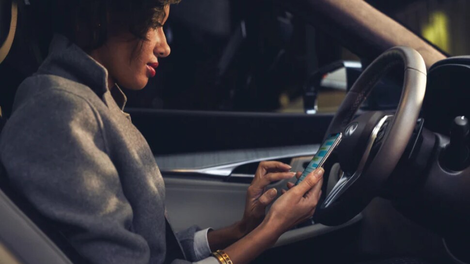 A woman using her phone to connect it to the 2023 INFINITI QX50
